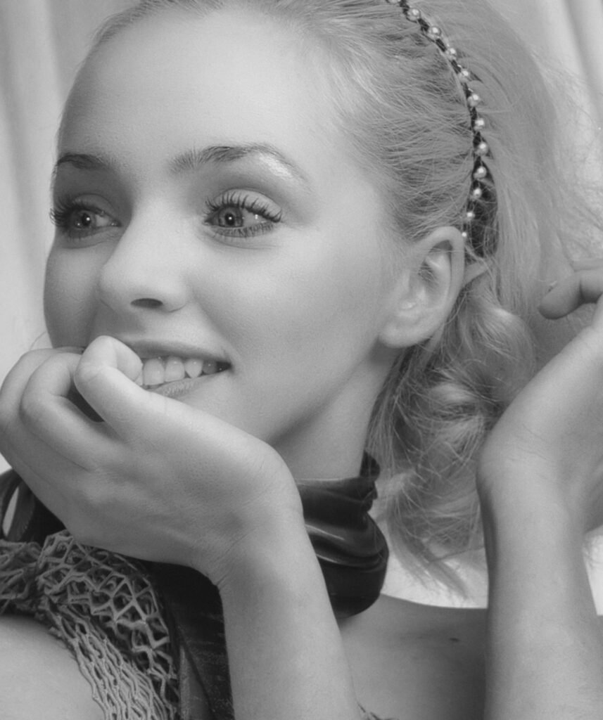 foto em preto e branco de uma mulher sorrindo com a mão no queixo arquinho no cabelo