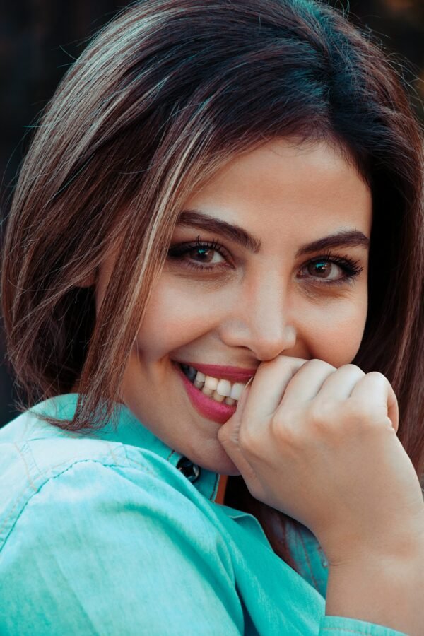 mulher sorrindo leve maquiagem batom vermelho cabelos castanhos lisos soltos uma das mãos na boca foto de Farshid Zabbahi unsplash.com