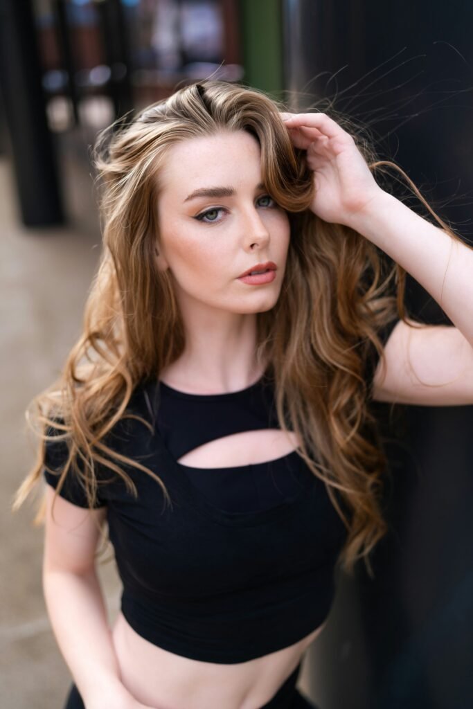 mulher maquiada olhos verdes cabelos longos lisos loiros blusinha preta uma das mãos nos cabelos