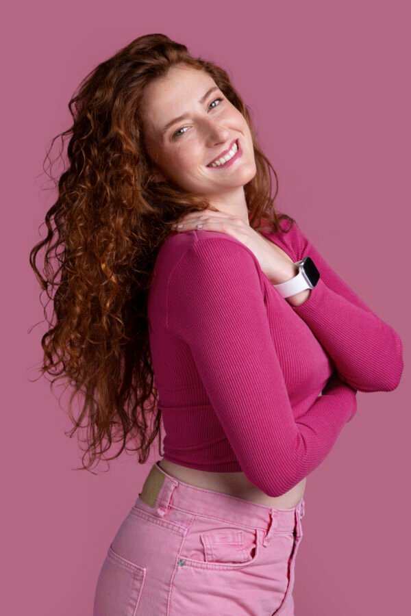 mulher ruiva sorrindo cabelos longos ondulados ruivos blusinha e calca cor rosa foto de freepik.com