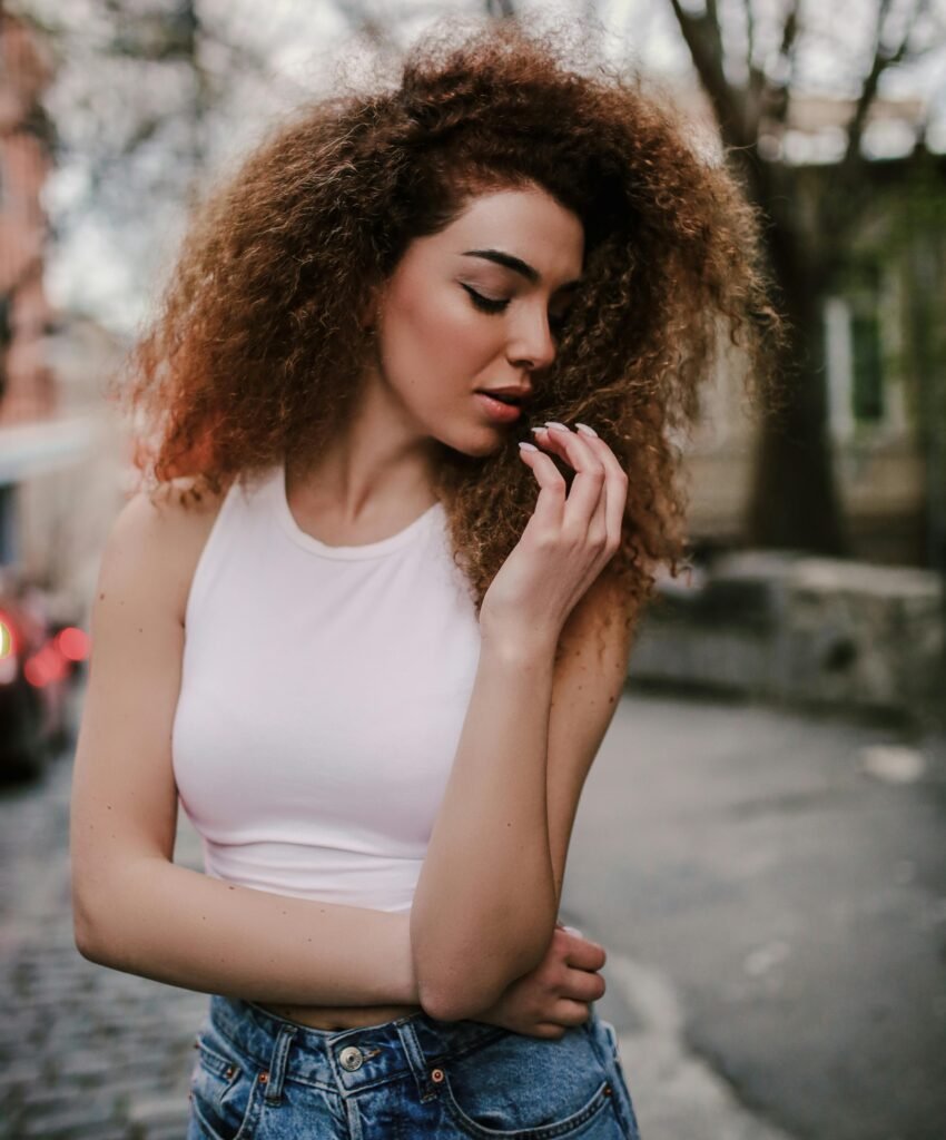 foto de mulher branca linda cabelos encaracolados grandes leve maquiagem uma das mãos nos celos camiseta branca