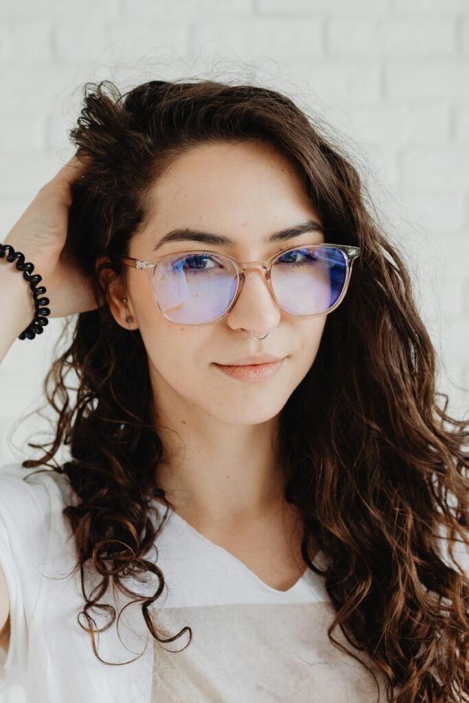 foto de perfil de mulher morena cabelos longos óculos e uma das mãos no cabelo