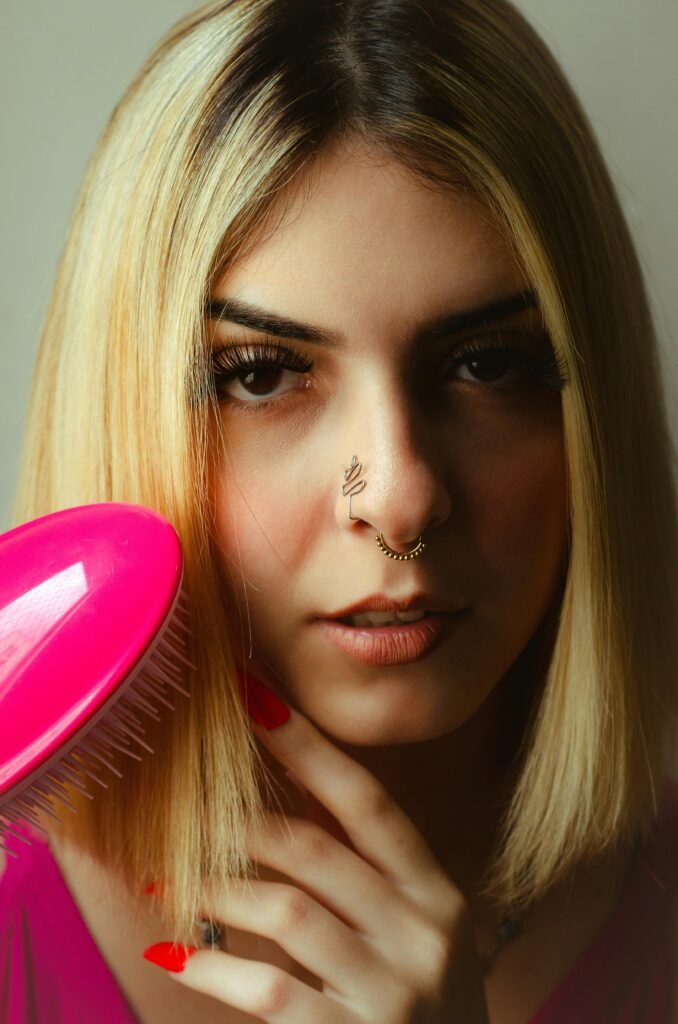 mulher loira cabelo bob cut chanel escovando os cabelos pente cor rosa pearcing no nariz unhas vermelhas