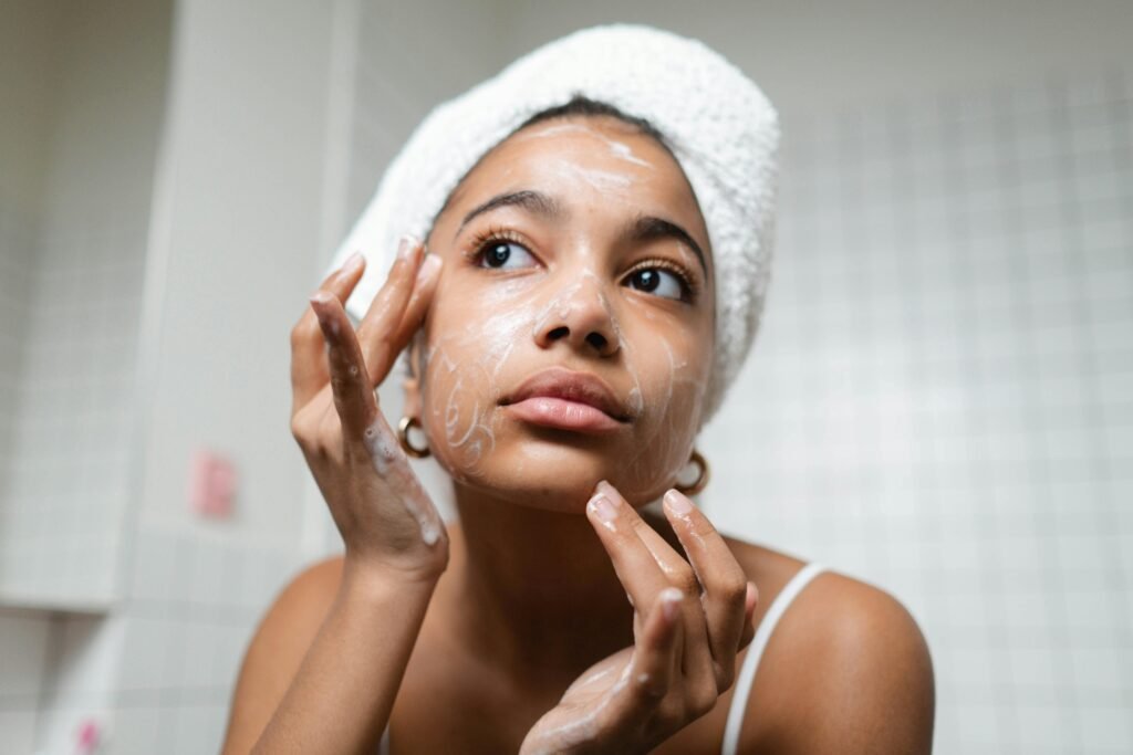 mulher morena com toalha no cabelo passando creme hidratante facial
