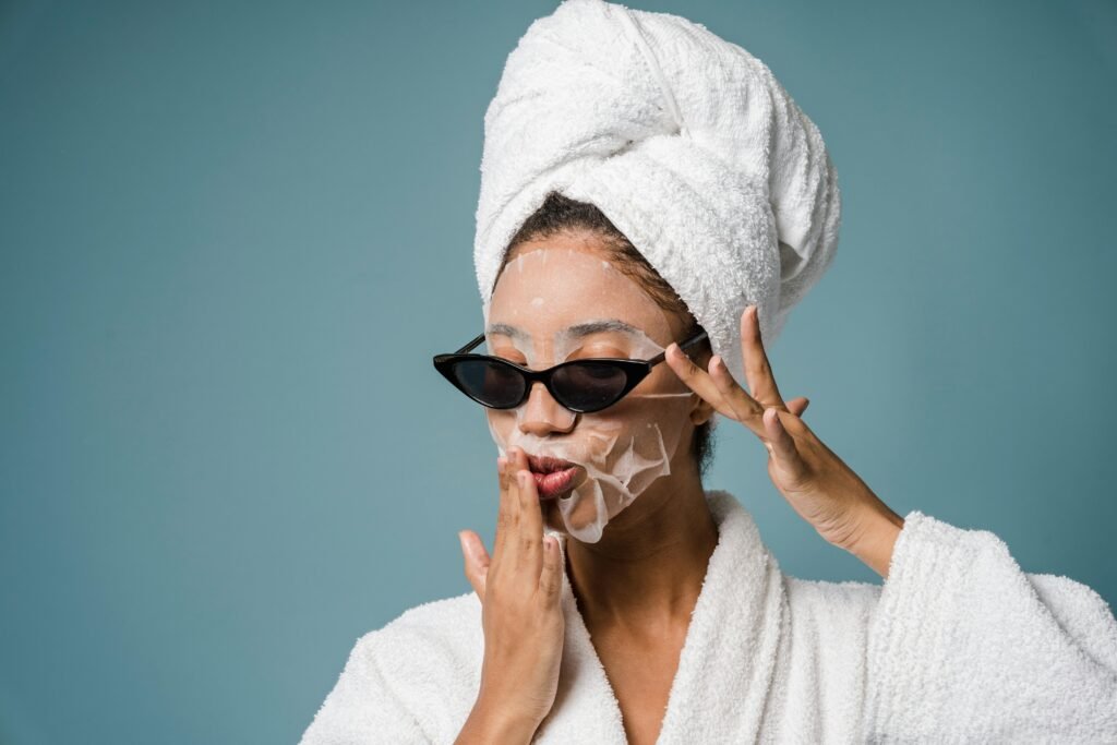 foto de mulher morena toalha na cabeça roupão de banho branco óculos estiloso preto mascara de hidratação no rosto mão na boca