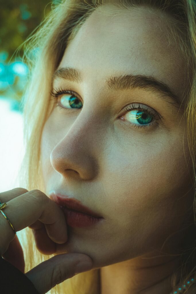 foto de perfil mostrando detalhes do rosto de uma mulher loira olhos verdes mão na boca