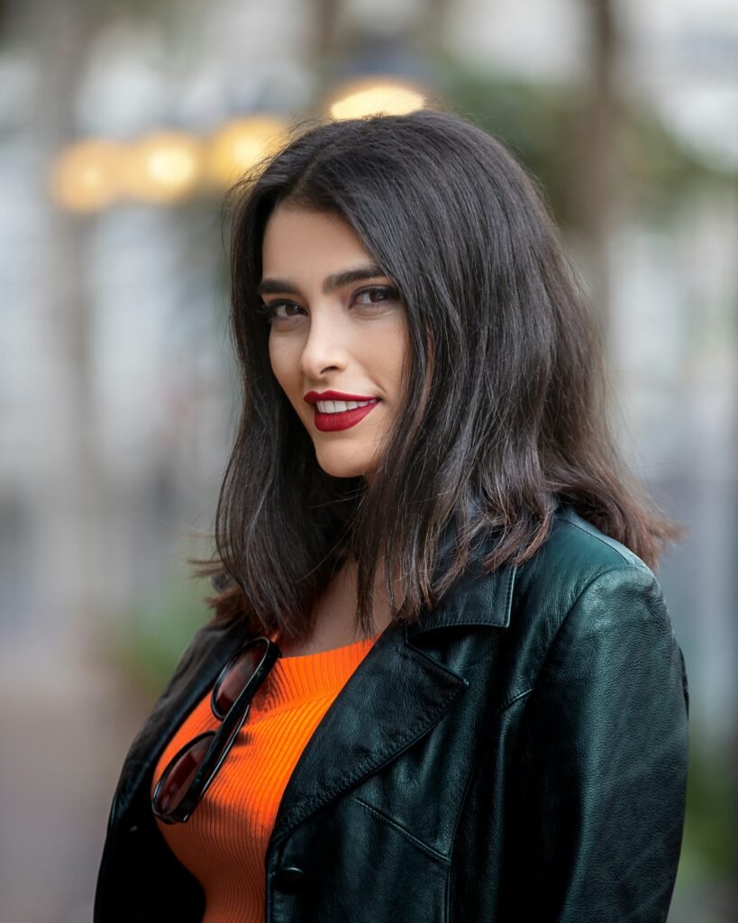 mulher sorrindo batom vermelho cabelos pretos lisos nos ombros blusa em couro preta blusinha cor laranja