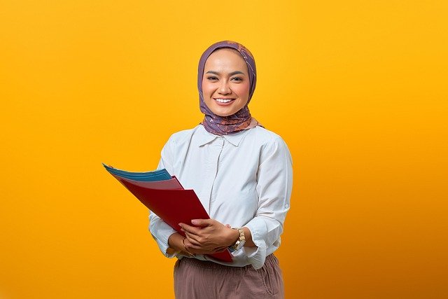 mulher sorrindo com hijab vestindo roupa social e segurando papeis