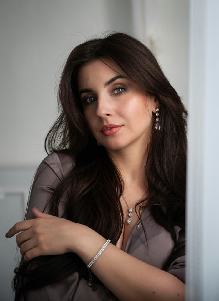 mulher maquiada olhos verdes brincos de brilhantes cabelos lisos longos pretos blusinha social cinza