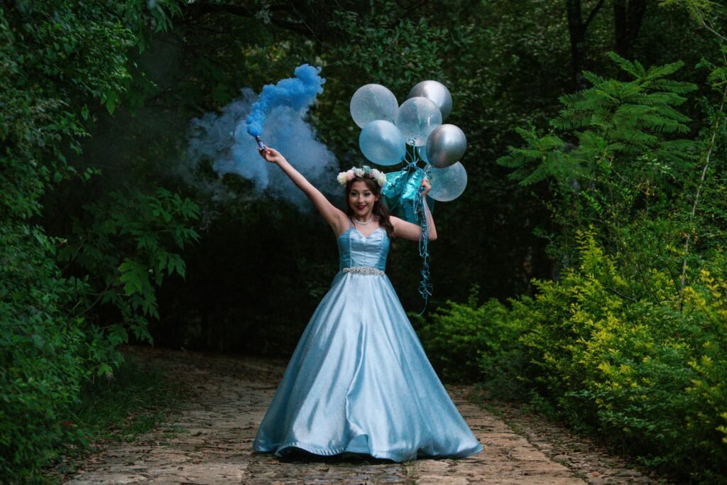 menina comemorando seus 15 anos, vestido de princesa cor azul claro metalizado segurando seis baloes e em outra mão segurando objeto que solta fumaça azul