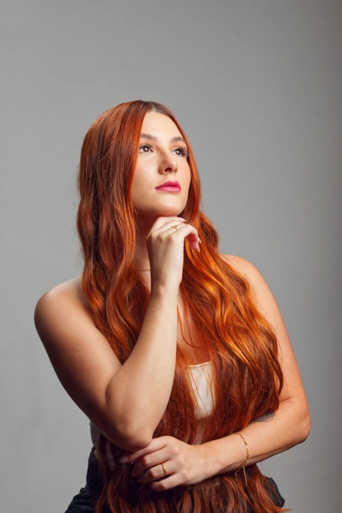 foto de mulher ruiva cabelos longos leve maquiagem uma das mãos no queixo