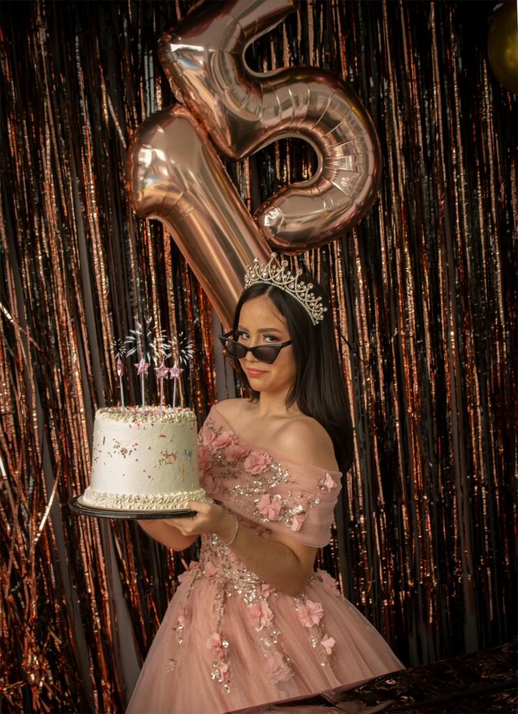 menina comemorando seus 15 anos, segurando um bolo lindo com velinhas, esta de óculos escuros leve sorriso e coroa de princesa no cabelo
