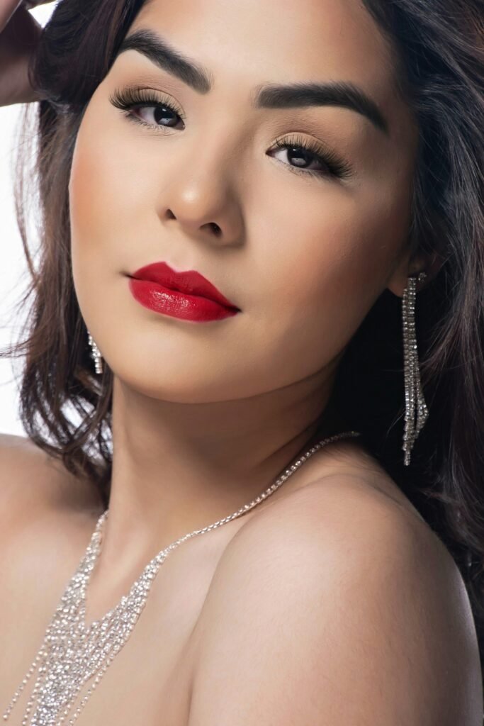 mulher maquiada batom vermelho cabelos lisos soltos pretos brincos e colar de brilhantes 