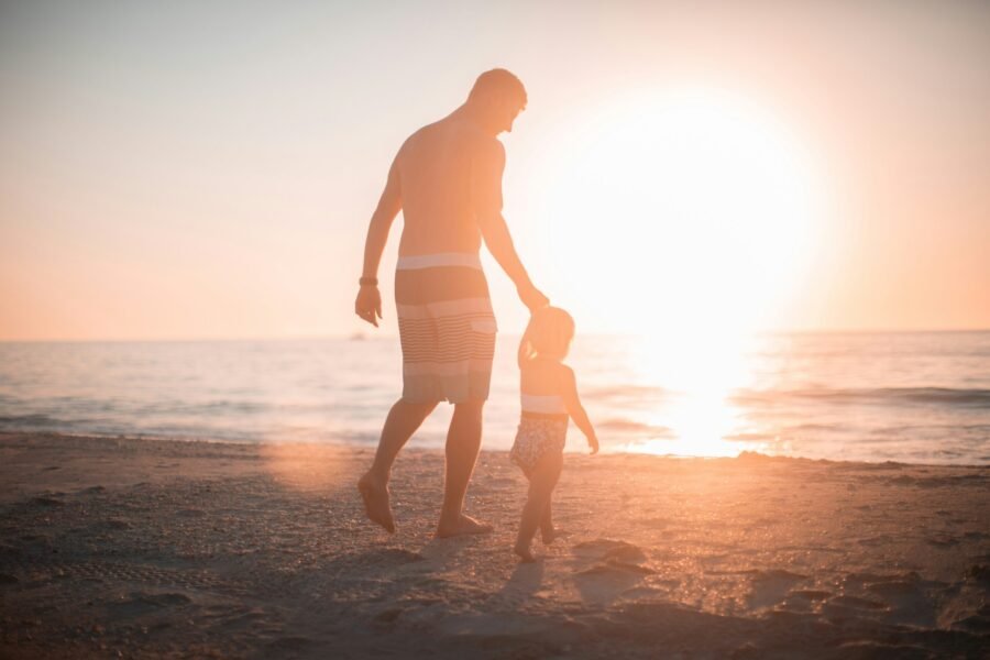 pai passeando na praia com sua filha pequenina ao por do sol foto de Derek Thomson unsplash.com