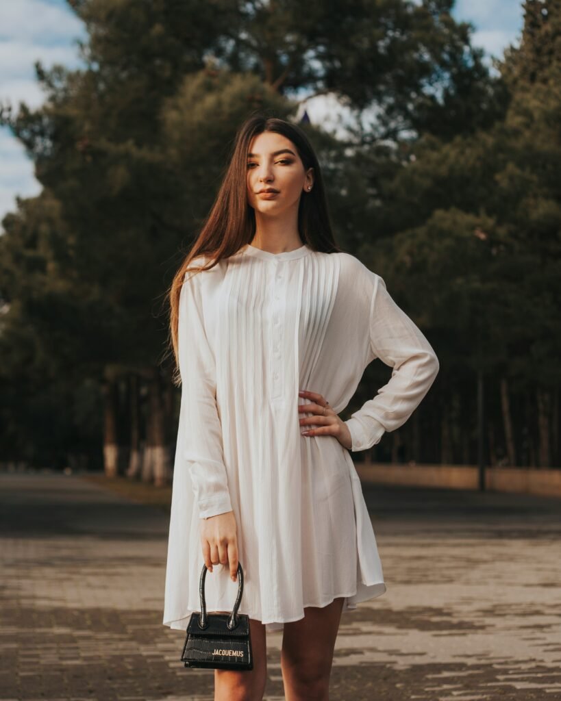 mulher cabelos longos lisos soltos mao na cintura blusinha grande branca estilosa vintage retro segurando uma bolsa pequena preta