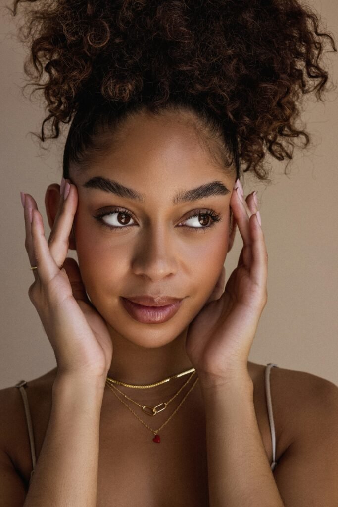mulher linda maquiada olhos castanhos duas mãos no rosto cabelos cacheados presos penteado coque