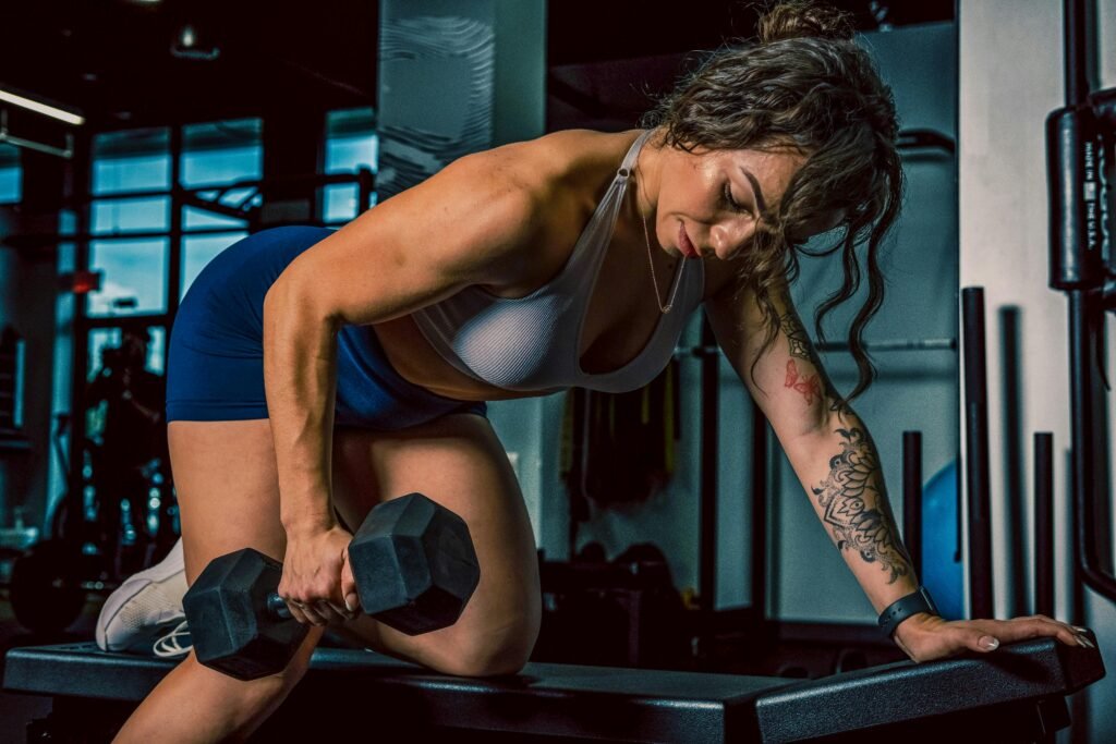 foto de mulher branca com tatuagem fazendo exercício em uma academia puxando peso