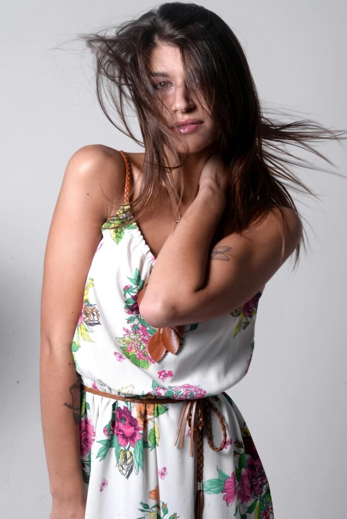 foto de mulher morena cabelos lisos longos espalhados uma das mãos no pescoço fazendo pose esta de vestido branco florido Shampoos que funcionam. Dicas de shampoos de farmácia