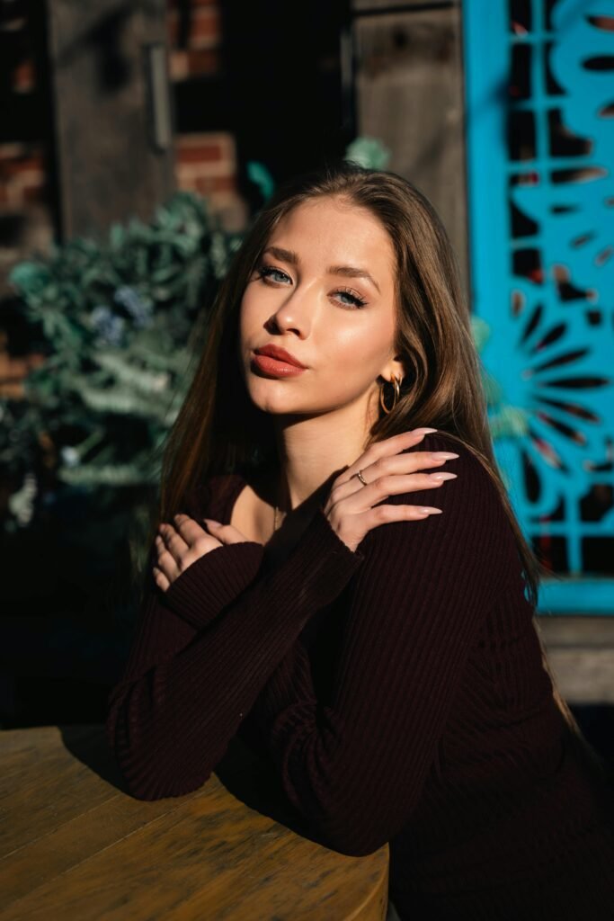 loira maquiada batom vermelho brincos argolas dourados olhos azuis bracos cruzados unhas estilosas grandes