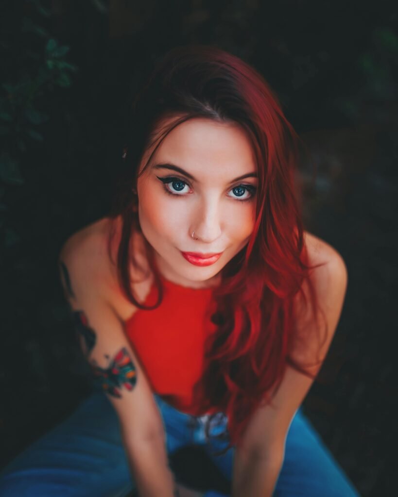 mulher jovem branca olhos azuis escuros, percingi no nariz cabelos longos vermelhos blusinha vermelha