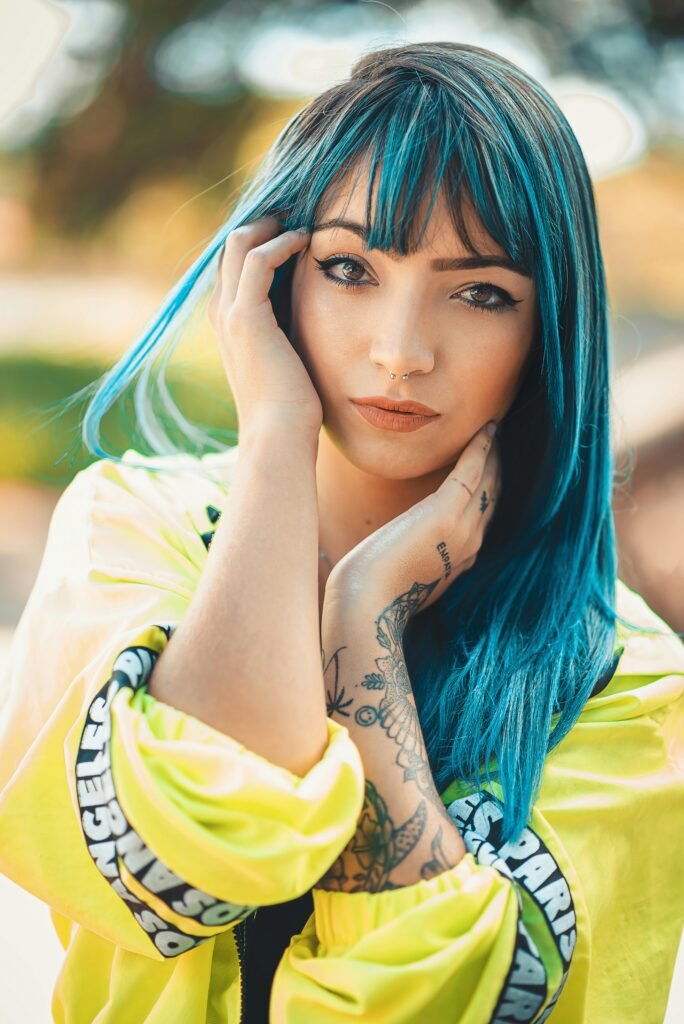 mulher morena cabelos lisos longos pintado de azul mãos no rosto e percingi no nariz