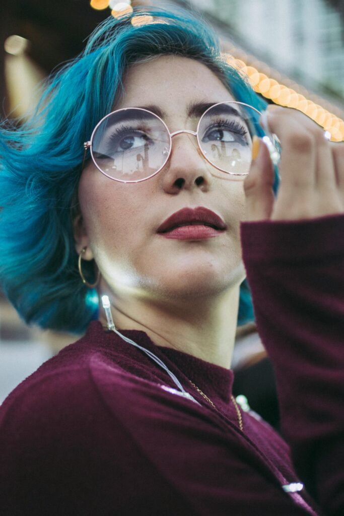 mulher maquiada oculos redondos e brincos argolas pequenos cabelos médio na cor azul