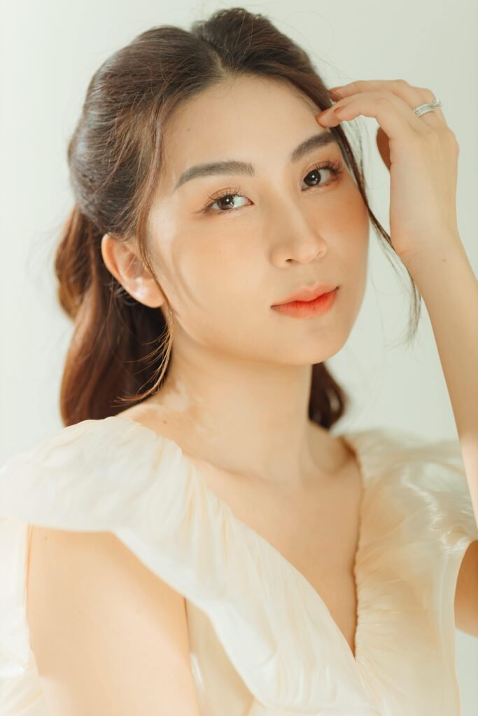 mulher jovem branca oriental leve maquiagem olhos castanhos cabelos compridos lisos, uma das mãos na cabeça dedos com anéis de prata