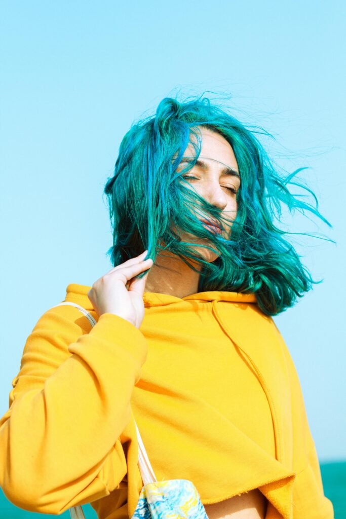 foto de mulher branca cabelo médio na cor azul uma das mãos segurando os cabelos blusa amarela