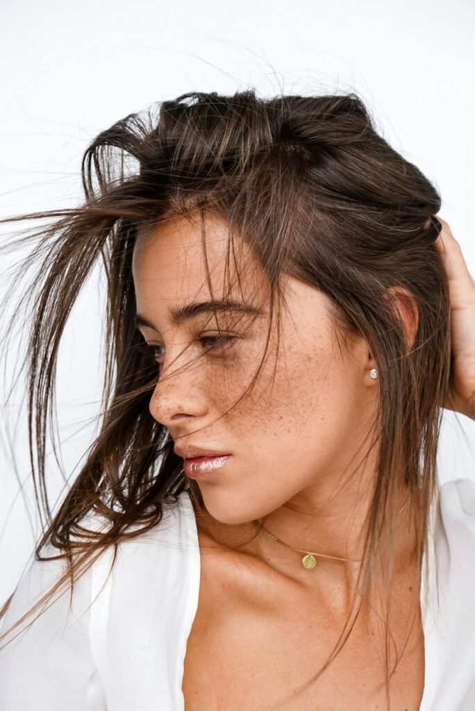 foto de mulher morena leve maquiagem brinco pequeno cabelos longos lisos espalhados mão na nuca fazendo pose