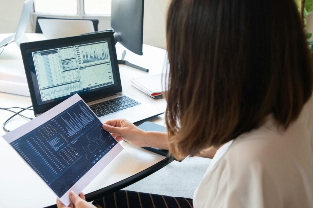 foto de uma mulher analisando gráficos estatísticos em uma folha de papel e em um notebook