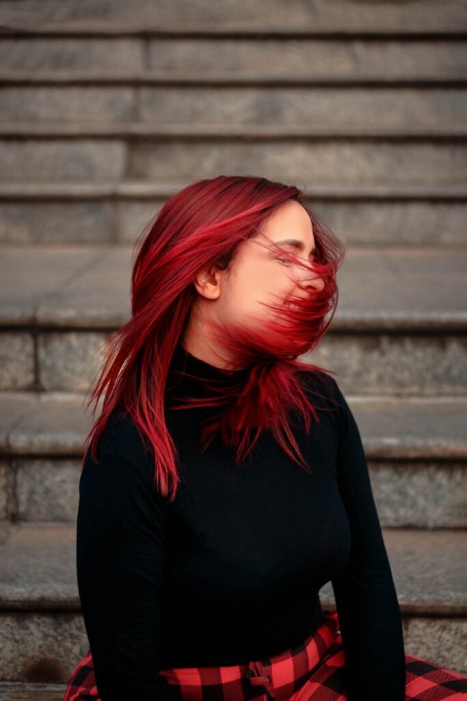 mulher jovem branca sorrindo blusa preta cabelos longos na cor vermelha, esta balançando os cabelos