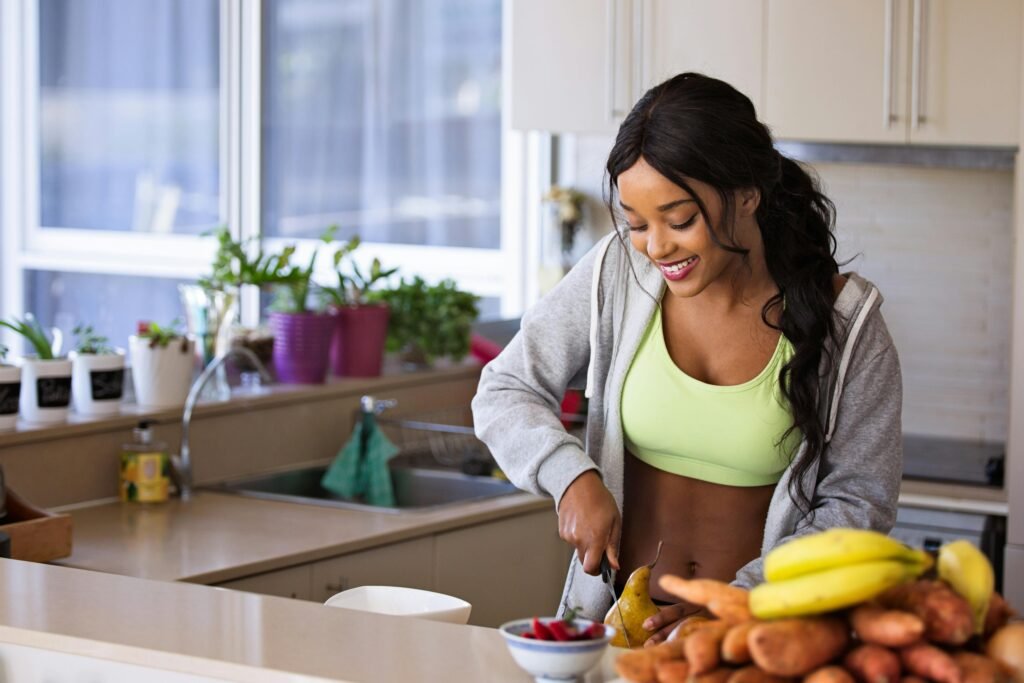 foto de uma mulher morena sorrindo cabelos compridos com roupa de academia cortando frutas na cozinha