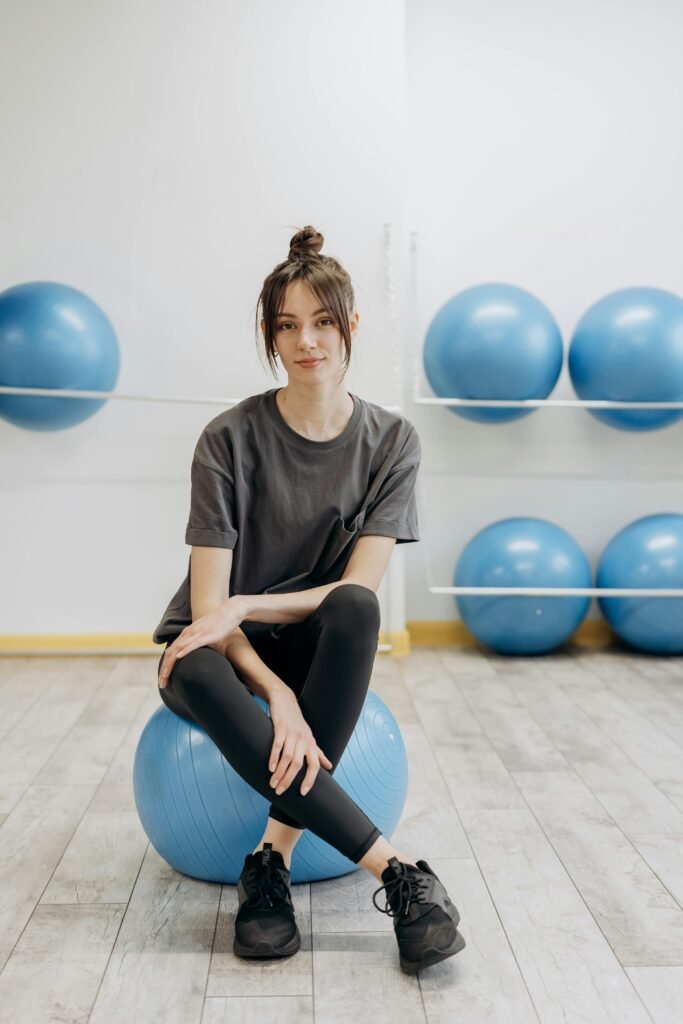 mulher sentada em uma bola grande azul para pratica de pilates