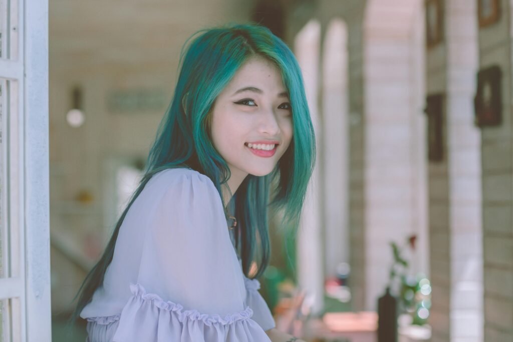 mulher branca jovem sorrindo cabelos compridos lisos na cor azul na janela