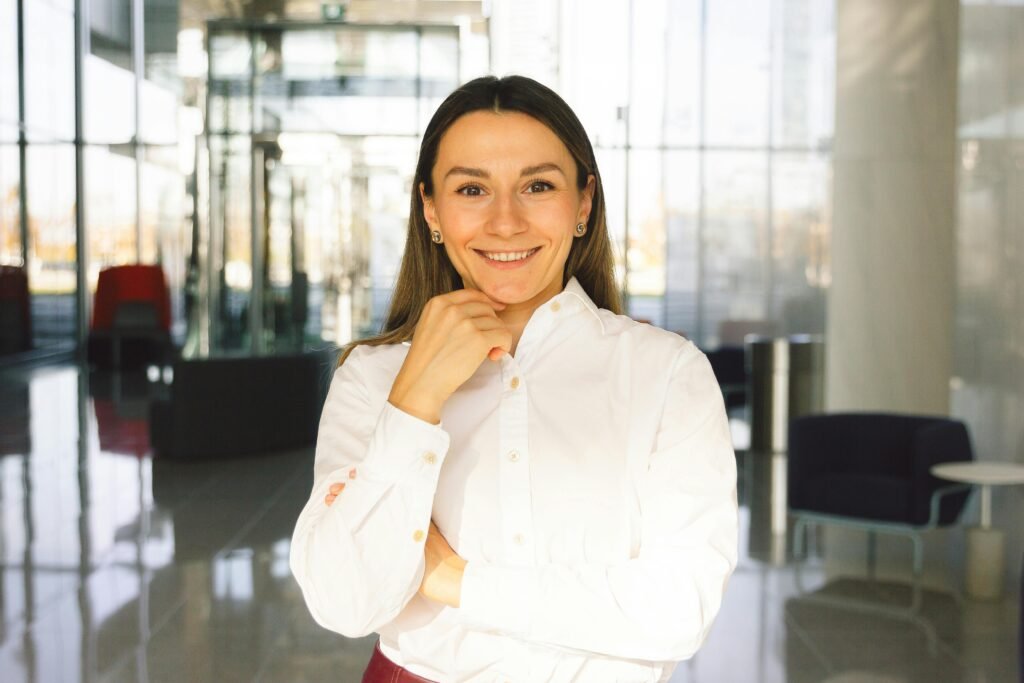 mulher branca sorrindo, de pé, um braco cruzado e outro com a mão próximo ao queixo. com brincos cabelos lisos longos