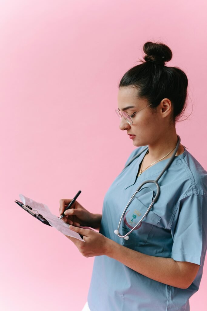 foto de uma mulher branca cabelos presos jaleco azul medica com estetoscopia fazendo anotações