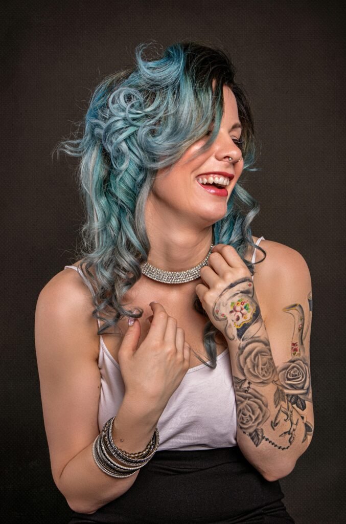 foto de mulher branca sorrindo colar de brilhantes cabelos compridos pintados de azul braco tatuado e pulseiras Pintar o cabelo de azul