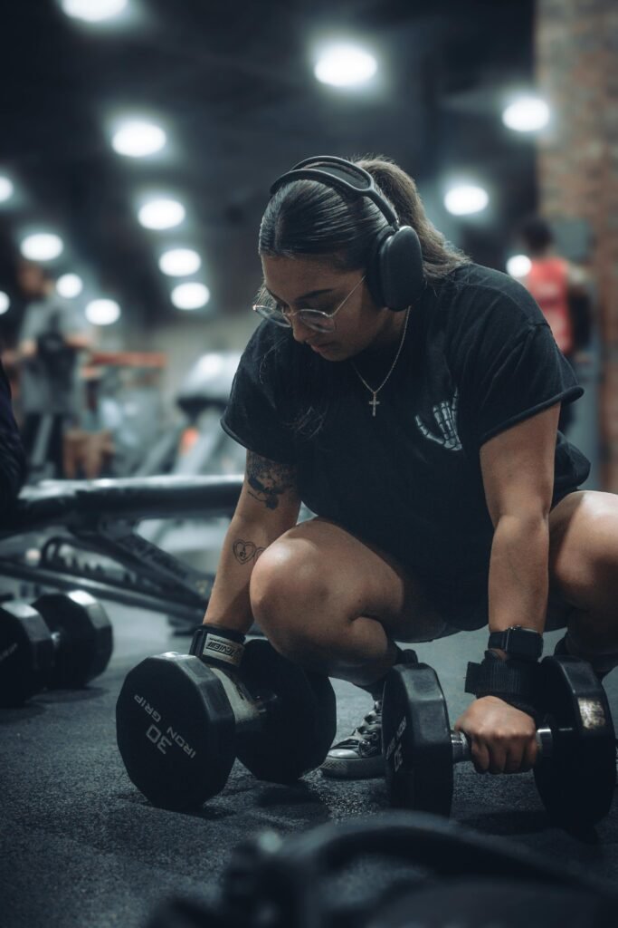 foto de mulher morena com fones de ouvido na academia levantando peso pra emagrecer roupa toda preta