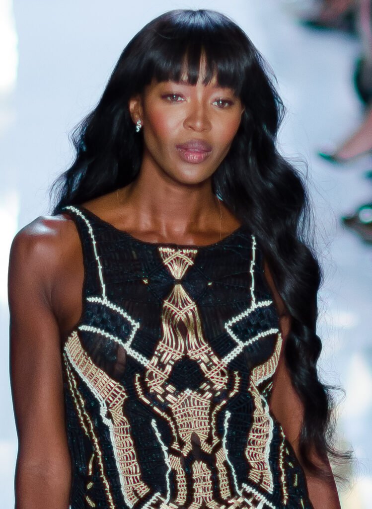 foto de Naomi Campbell linda maquiada cabelos longos lisos soltos penteado franja olhos castanhos vestido estiloso preto bordado detalhes em prata e dourado