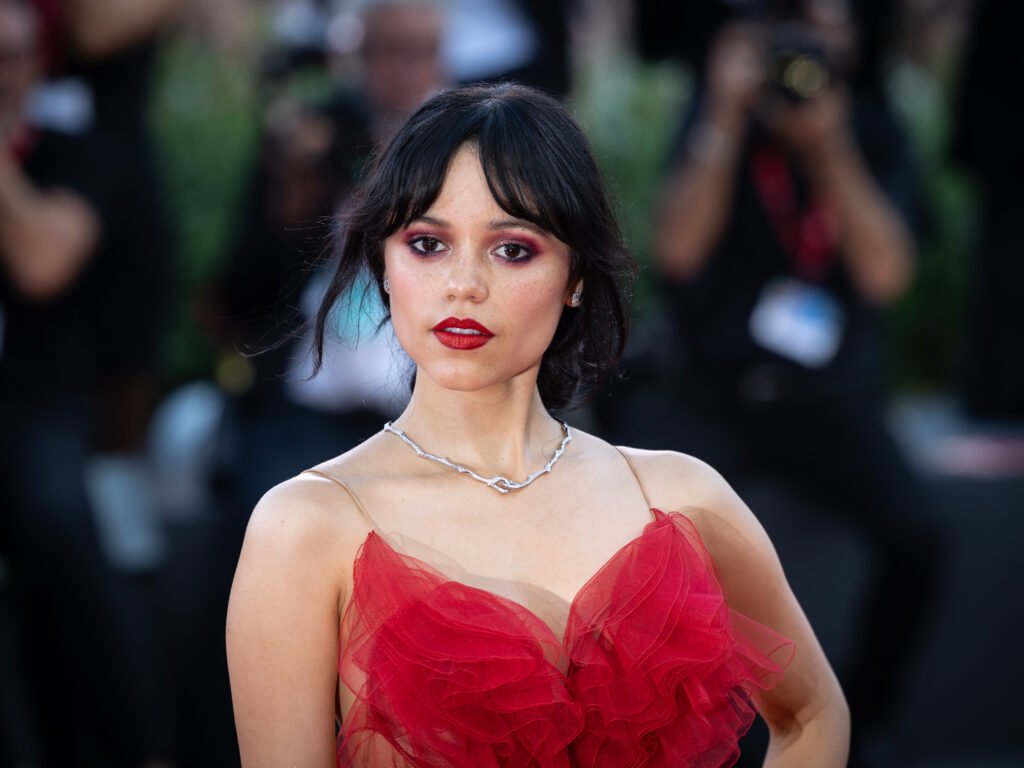 foto de Jenna Ortega linda cabelo Halo Fringe maquiada batom vermelho vestido estiloso de festa vermelho colar estiloso de prata