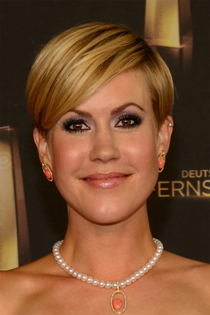 foto de mulher Wolke Hegenbarth sorrindo maquiada olhos castanhos brincos pequenos cor laranja cabelo curto pixie estiloso colar de perolas