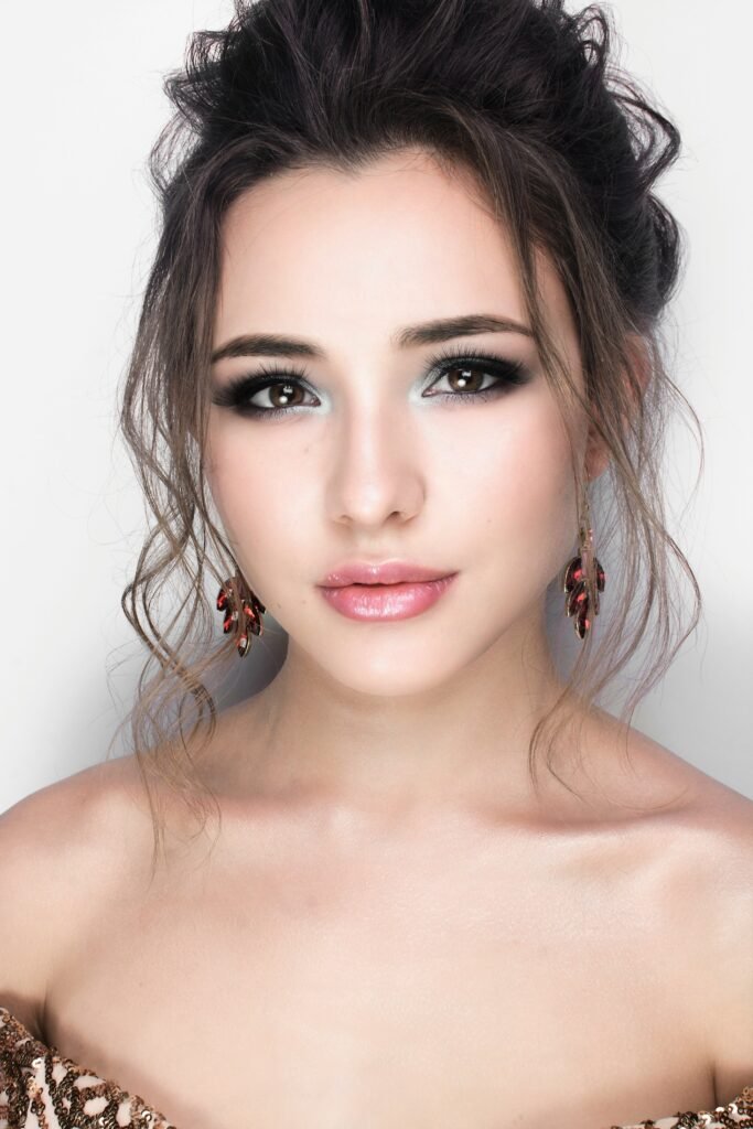 mulher maquiada leve sorriso penteado cabelos presos coque com duas mexas na frente brincos desenho de folha