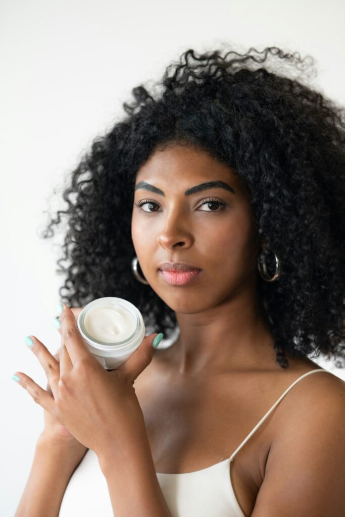 mulher linda cabelos crespos longos brincos argolas prata olhos castanhos segurando um pote de creme de hidratação