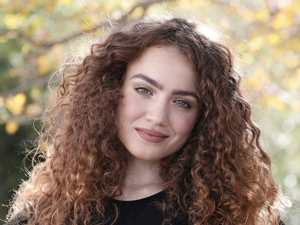 mulher sorrindo olhos verdes claros cabelos longos volumosos cacheados castanhos blusinha preta