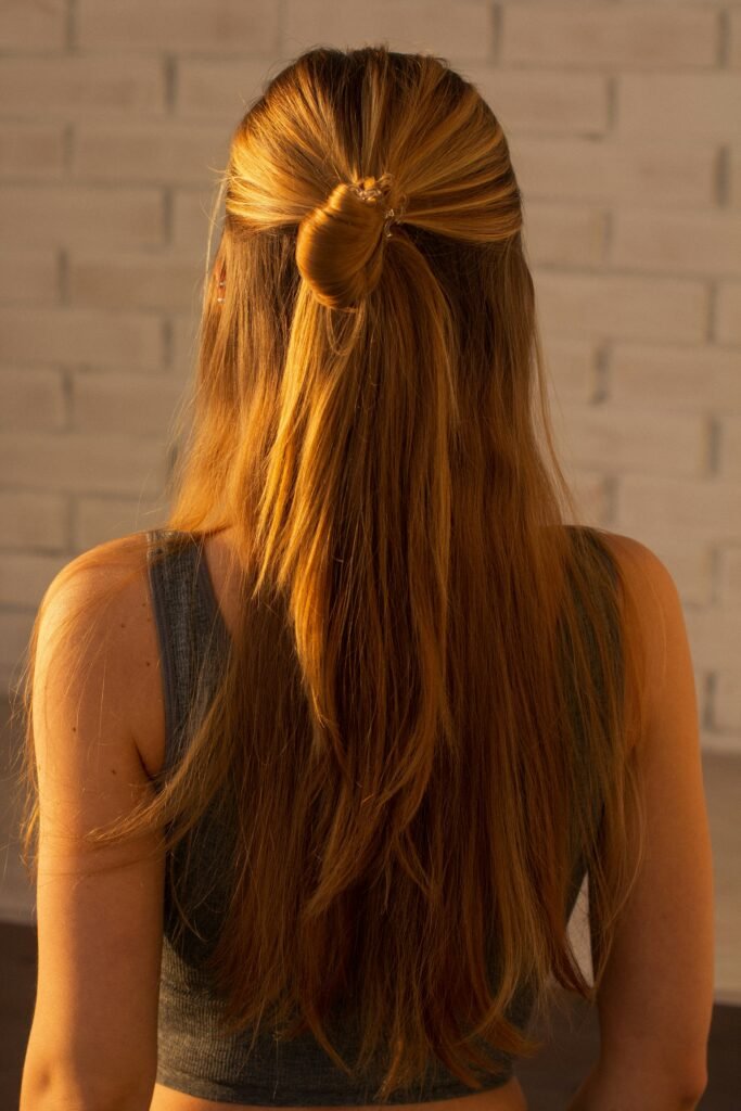 mulher de costas cabelos longos lisos loiros com penteado coque e rabo de cavalo blusinha cinza