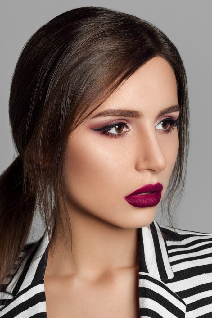mulher maquiada batom roxo cabelos lisos preso camisa estilosa listrada de preto e branco