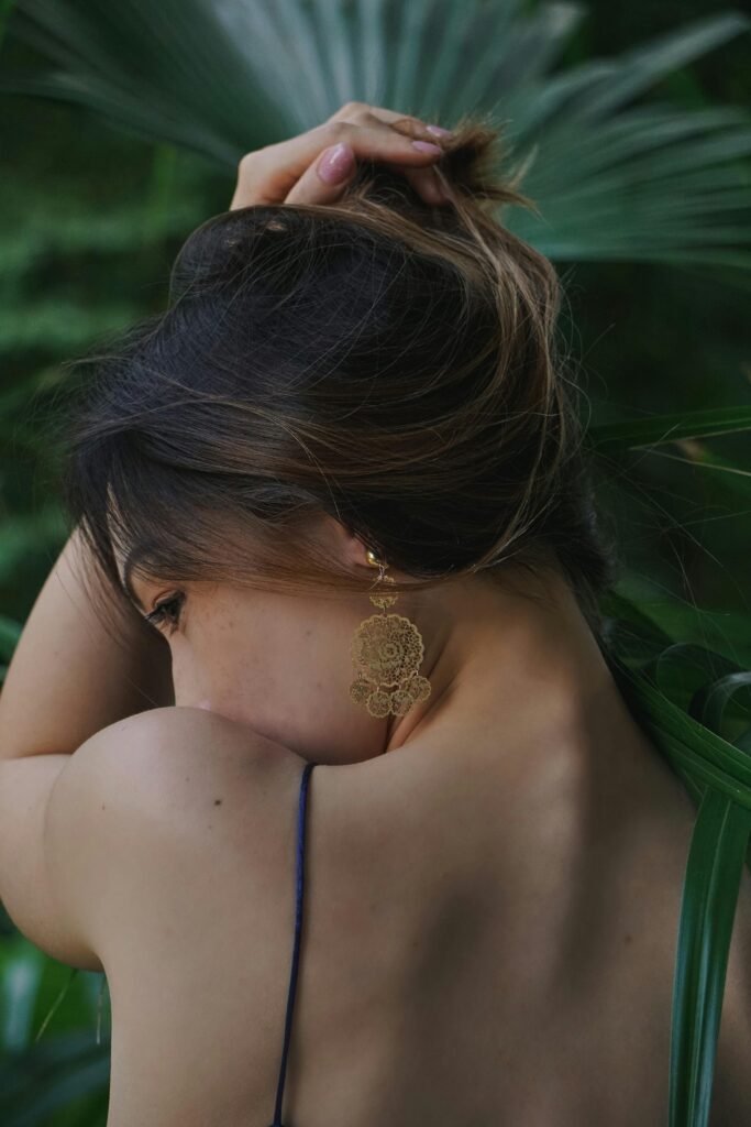 foto de mulher morena de costas cabelos lisos presos french hair pin uma das mãos nos cabelos leve olhar pra trás brinco grande