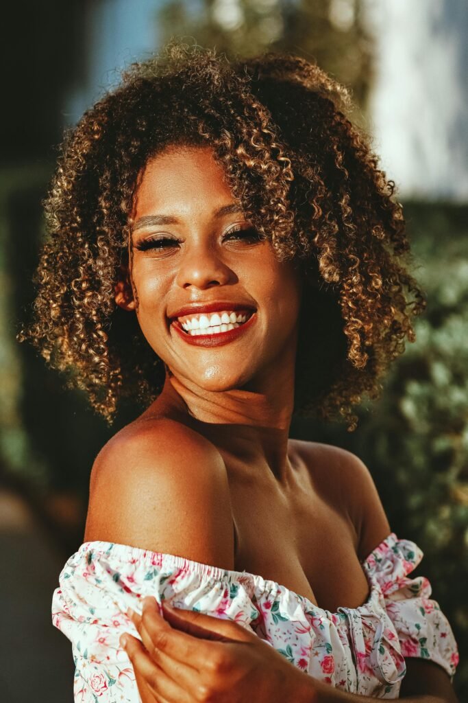 foto de perfil de mulher preta linda sorrindo cabelos cacheados 3c blusinha florida branca