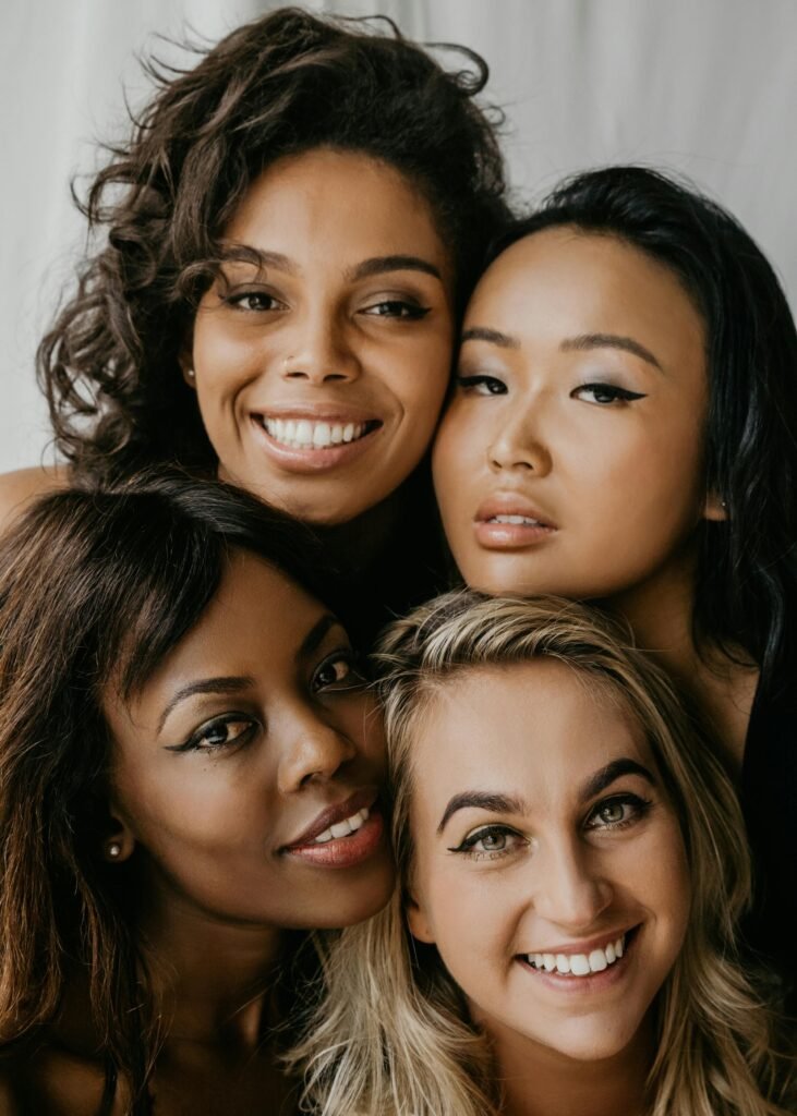 foto do rosto de quatro mulheres diferentes juntas sorrindo leve maquiagem branca preta oriental morena
