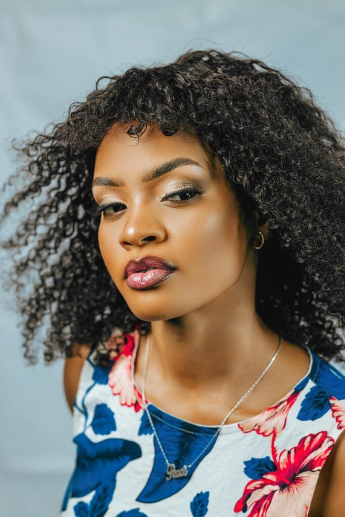 mulher preta linda maquiada olhos pretos brincos pequenos cabelos crespos grandes batom roxo vestido florido